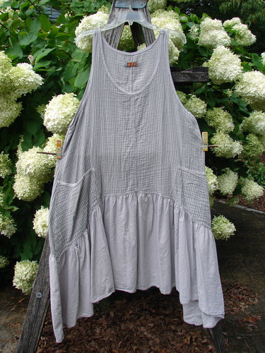 Barclay Gauze Batiste Summer Frock Jumper Stripe Light Stone Size 1, a light stone striped sleeveless frock with a rounded neckline, soft gauze batiste texture, and a gathered lower panel. It hangs centered on a wooden frame amid white hydrangeas and deep green foliage.