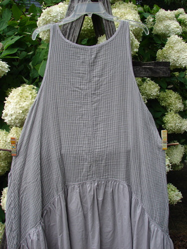 Barclay Gauze Batiste Summer Frock Jumper Stripe Light Stone Size 1 in light stone, a sleeveless gauze batiste dress with fine vertical stripes, a rounded neckline, and a gathered lower panel. The soft, airy fabric hangs from a hanger against dense white hydrangeas and dark greenery.