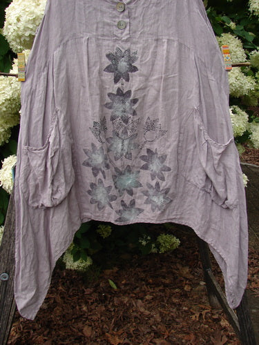 Bluefishfinder.com Barclay Linen Tuesday's Dress Majestic Petal Mallow, size 0, in a soft mauve linen with a loose drape, buttoned neckline, and gathered sleeves. A muted floral print runs down the front, while the hem falls unevenly in a layered, airy silhouette.