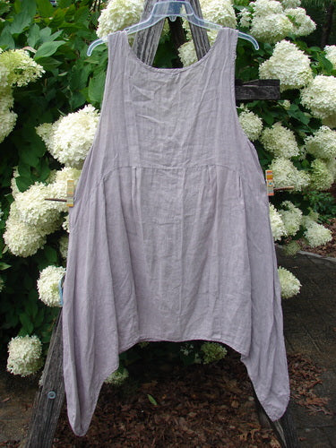 Bluefishfinder.com Barclay Linen Tuesday's Dress Majestic Petal Mallow, size 0, is a sleeveless linen dress in soft mauve-gray with a loose, draped silhouette, wide arm openings, and a gently curved hem. It hangs against white hydrangeas, emphasizing its airy texture and relaxed shape.