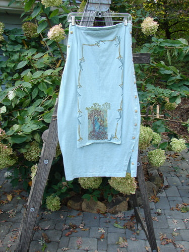 1994 Apron Skirt Magic Garden Menthe Size 1 displayed on a wooden ladder, highlighting its layered design, unique painted apron panel, and vertically curved side buttons, reflecting vintage Blue Fish Clothing style.