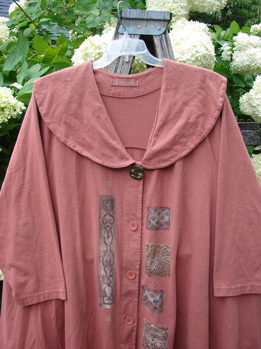 Bluefishfinder.com 1994 Wanderer's Jacket Continuous Garden Monrovian Brick Size 2 in muted brick rose, a loose, collarless jacket with a draped shawl-like neckline and front buttons. It hangs from a clear hanger against leafy hydrangeas, its soft fabric marked by vertical patterned panels.