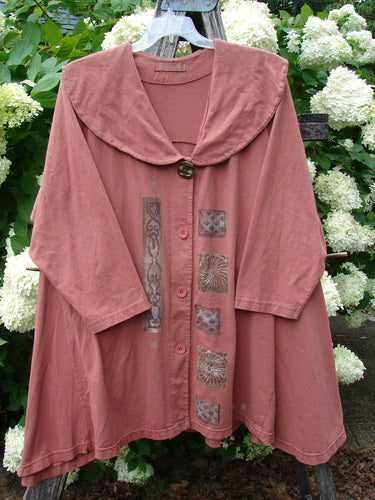 Bluefishfinder.com 1994 Wanderer's Jacket Continuous Garden Monrovian Brick Size 2 in muted brick pink, a loose, cape-like jacket with a broad sailor collar, button front, and printed vertical panels. The soft, matte fabric hangs in gentle folds against white hydrangeas and green leaves.