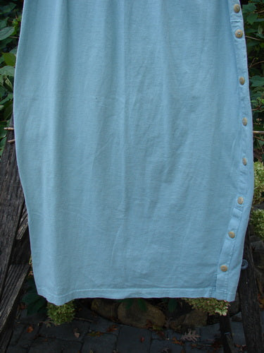 1994 Apron Skirt Magic Garden Menthe Size 1 displayed outdoors, showcasing its unique vertical buttons and artistic painted apron panel, set against a wooden fence, reflecting vintage elegance from the 1994 Spring Collection.