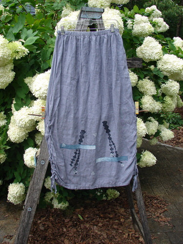 Bluefishfinder.com 1997 Breeze Skirt Sealife Naya Size 1 in faded blue-gray fabric, shown as a long gathered skirt with a soft drape, side ties, and small sea-life motifs near the hem, hanging outdoors against white hydrangeas and weathered wood.