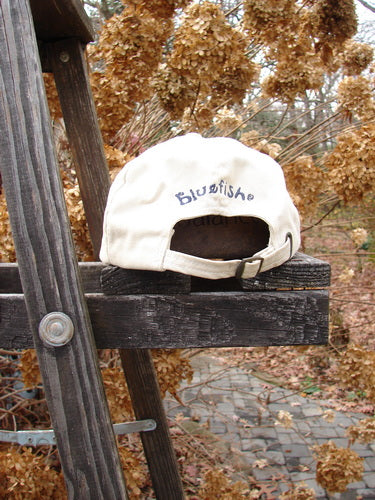 1999 Patched Men's Baseball Cap Single Fish BF Logo Natural OSFA, displayed on a wooden ladder. The cap features blue writing, adjustable rear strap, and distinct sectional star stitchery.