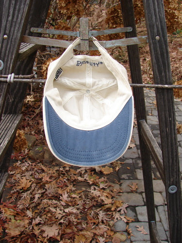 1999 Patched Men's Baseball Cap Single Fish BF Logo Natural OSFA displayed on a ladder, highlighting the adjustable rear tan strap with a metal snap-down clip and the cloth-covered top center button.