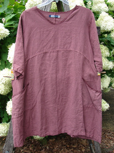 Barclay Summercloth Ditsy Trim Urchin Dress in unpainted loam, large size 0, shown as a loose mauve-brown dress with a soft, crinkled texture, rounded neckline, elbow-length sleeves, and curved seam details. It hangs centered on a wooden hanger against leafy greenery.