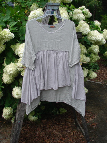 Barclay Gauze Batiste Petal Urchin Flounce Dress in unpainted rice paper, size 1, hangs from a wooden ladder against white hydrangeas and green foliage. The loose gauze layers, soft drape, and uneven flounced hem give it a light, airy texture.