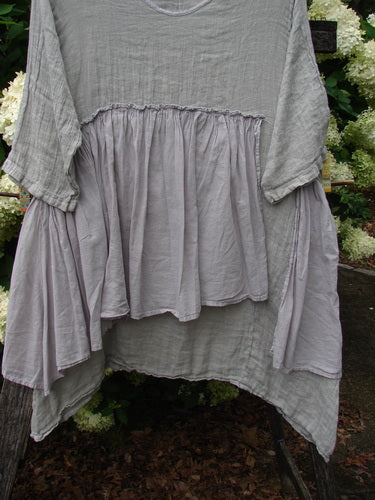 Barclay Gauze Batiste Petal Urchin Flounce Dress in unpainted rice paper, size 1, shown in soft gray gauze with a loose, oversized silhouette. The dress has a gathered flounce panel across the front, wide draped sleeves, and a lightly crinkled, airy texture.