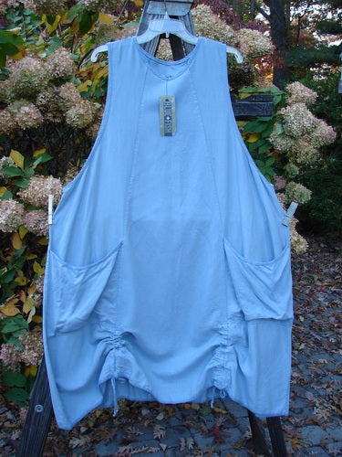 Barclay NWT Twill Joyous Jumper Unpainted Sky Size 2 hanging on a clothesline, showcasing deep arm openings, double drop front exterior pockets, and dual hem drawcords for a sweeping A-line shape.