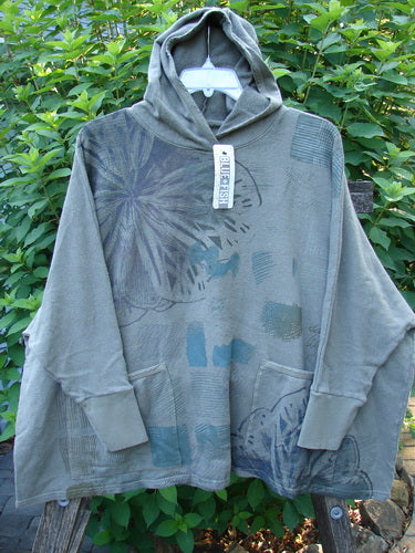 Barclay NWT Cotton Hemp Hooded Folklore Pullover Blossom Grey Lolite OSFA displayed against a rustic wooden fence, showcasing its cordless hood, ribbed cuffs, and dual painted pockets from the Fall Collection.
