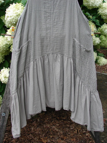 Barclay Gauze Batiste Summer Frock Jumper Stripe Sand Stone Size 1 in soft gray striped gauze batiste, with a loose sleeveless silhouette, gathered dropped waist, and wide ruffled hem. The lightweight fabric hangs in layered folds, centered against an outdoor garden backdrop.