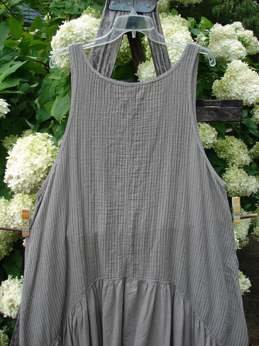 Barclay Gauze Batiste Summer Frock Jumper Stripe Sand Stone Size 1 in muted gray, with a sleeveless scoop neckline and fine vertical stripes that give the gauzy batiste fabric a subtle ribbed texture. The dress hangs from a clear hanger against white hydrangeas and dark wood, with a softly gathered lower panel and airy, lightweight drape.