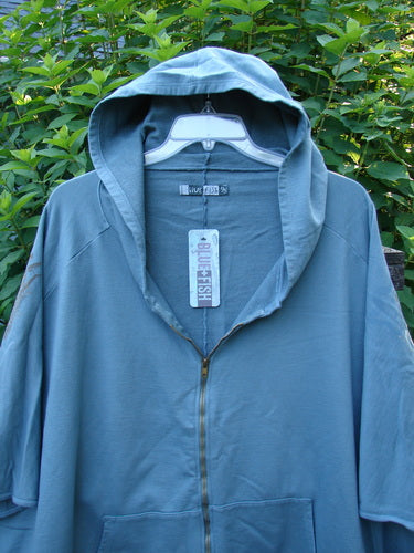 Barclay NWT Hooded Postcard Zipper Jacket Vest Rear Tree Love Delaware Green OSFA displayed outdoors, featuring a cozy hood, full zipper, dolman shoulders, and unique tree-themed rear design on a swinging hanger.