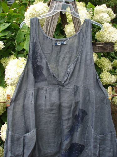 Barclay Linen Tuesday's Dress in Guinea Feather Grey Storm, size 0, is a sleeveless linen dress with a scooped neckline, soft drape, and dark featherlike print. The gray fabric hangs from a clear hanger, with gathered seams and side pockets.