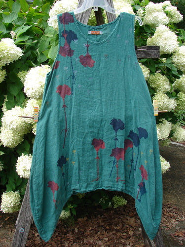 Barclay Linen Round Bottom Pinafore in Cloud Burst Jade, size 0, is a sleeveless teal linen dress with a round neckline and softly curved hem. Maroon and navy floral stems scatter across the front, hanging against a rustic outdoor backdrop.