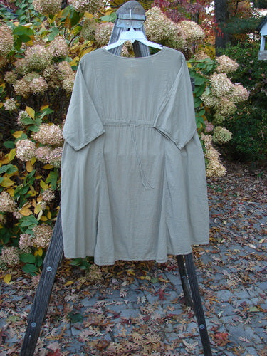 Barclay NWT Batiste Bliss Dress Fallen Petal Dovetail Size 2 displayed on a wooden stand, showcasing its rounded neckline, short sleeves, front pockets, and artistic center section.