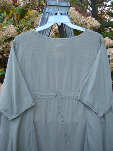 Barclay NWT Batiste Bliss Dress Fallen Petal Dovetail Size 2 displayed on a metal swinger with a wooden stand, showcasing short sleeves, two exterior pockets, and a drawcord back.