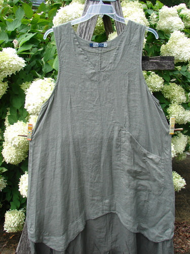 Barclay Linen Explorer Jumper in Buttercup Green River, size 0, hangs from a clear hanger against a backdrop of white hydrangeas and green leaves. The sleeveless linen piece has a softly wrinkled texture, a scoop neckline, and a loose, layered hem.