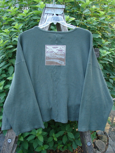 Barclay Patched Thermal Donna Top Out West Deep Army OSFA features drop shoulders, belled sleeves, and a wide rounded neckline. Showcased on a wooden hanger, highlighting its unique waffle texture and patch detail.