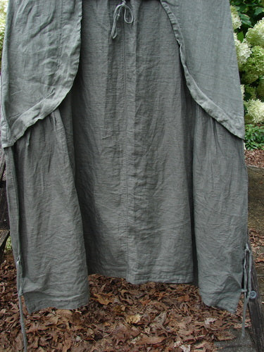 Barclay Linen Explorer Jumper in Buttercup Green River, size 0, made of crinkled linen with a draped, layered silhouette. The long garment hangs open to reveal a loose central panel and rounded side panels, rendered in muted green-gray tones.
