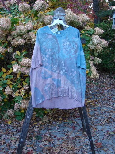 Barclay NWT Tournesol Top Abstract Floral Denim Amethyst OSFA, displayed on a rack, showcasing its tunic length, drop shoulders, three-quarter sleeves, rounded neckline, and varying hemline with a floral motif.