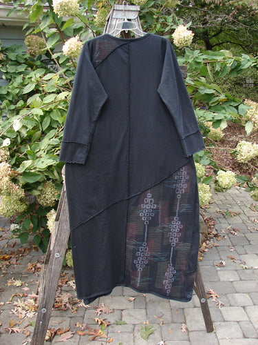 Barclay Diagonal Pocket Dress Stick Stone Black Size 0, featuring a long A-line design, curly sleeves, and a diagonal pattern. Displayed on a wooden rack, showcasing its elegant organic cotton craftsmanship.