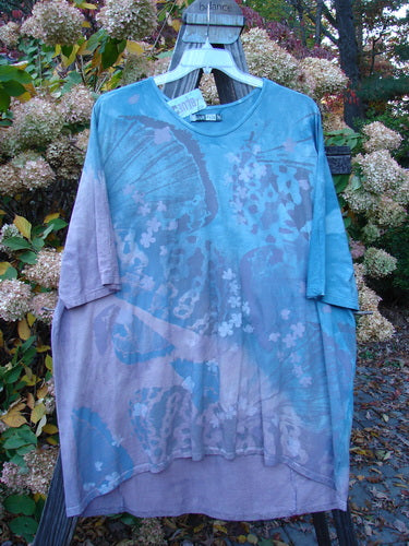 Barclay NWT Tournesol Top Abstract Floral Denim Amethyst OSFA displayed on a hanger with a butterfly design and three-quarter sleeves, featuring a varying hemline, longer in the back than the front.
