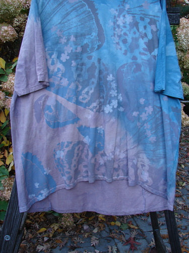 Barclay NWT Tournesol Top Abstract Floral Denim Amethyst OSFA displayed on a rack, showcasing its tunic length, drop shoulders, loose three-quarter sleeves, and varying hemline.