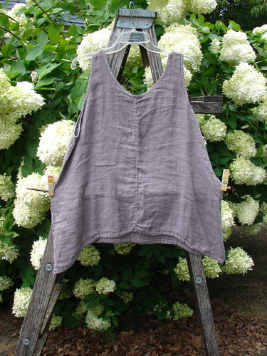 Barclay Linen Altoll Top Wing Stats in rose quartz, size 0, shown as a sleeveless linen top with a softly crinkled texture, wide straps, and a relaxed A-line drape. It hangs from a weathered wooden ladder amid dense white hydrangeas and deep green foliage.