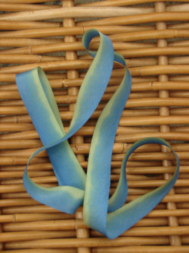 Blue Fish Hand Dyed Silk Ribbon in Sea Goddess 108 x 5/8th, displayed on a woven wicker surface, showcasing its light, flowing texture and unique hand-dipped color variance.