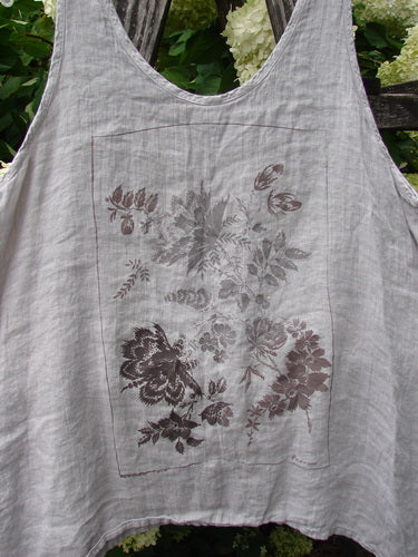 Barclay Linen Altoll Top Floral Victorian Floral Natural Size 0 is a sleeveless natural linen top with a soft, crinkled texture and a wide scoop neckline. A rectangular floral Victorian print sits centered on the front in muted gray and plum tones, against a leafy outdoor backdrop.