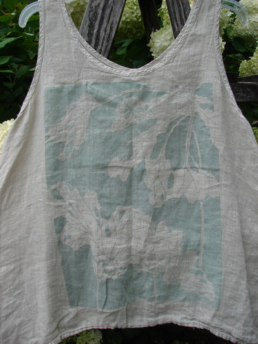 Barclay Linen Altoll Top Blossom Reach Creme Size 0, a sleeveless linen top with a rounded scoop neckline and soft cream base. A faded blossom print in pale teal and white spans the front, while the lightweight, crinkled fabric hangs against a leafy outdoor backdrop.