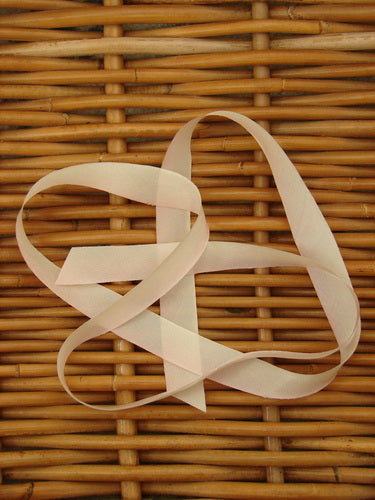 Blue Fish Hand Dyed Silk Ribbon in Peach Blossom 108 x 5/8th displayed on a woven wicker basket, highlighting its delicate, light, and flowing texture, perfect for vintage Blue Fish clothing adornments.