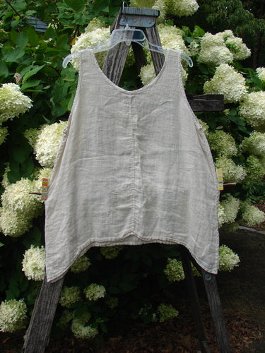 Barclay Linen Altoll Top Blossom Reach Creme, a sleeveless size 0 linen top in soft cream, with a relaxed A-line shape, raw-edged hem, and subtle vertical seam detail. It hangs from a wooden ladder amid white hydrangea blooms and deep green foliage.