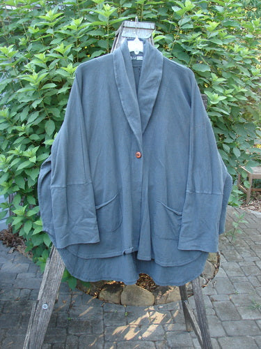 Barclay Reprocessed Golden Hour Deco Jacket Rear Rain Black Olive OSFA draped elegantly on a fence, showcasing its single button closure, long sleeves, and distinctive flowing varying lengths.