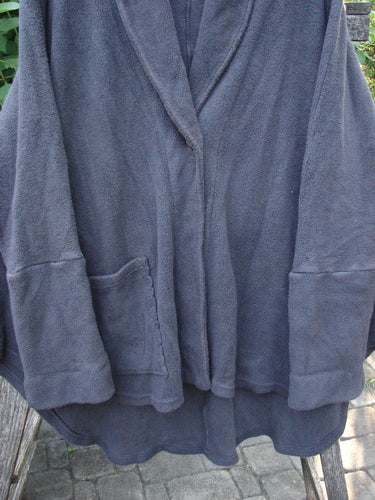 Barclay Patched Celtic Moss Deco Coat Unpainted Stormy Black OSFA displayed on a wooden pole, showcasing its dense textured feel, oversized vintage button, drop dolman shoulders, and deep V neckline with a stand-up collar.