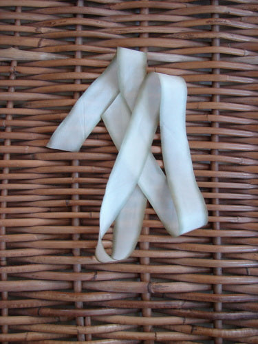 Blue Fish Hand Dyed Silk Ribbon in Sweet Meadow 108 x 1, displayed on a woven wicker surface, showcasing its light, flowing texture and unique color variance.