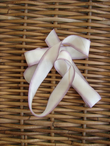 Blue Fish Hand Dyed Silk Ribbon in Wisteria Walk 108 x 1 displayed on a woven wicker surface, showcasing its light, flowing texture and unique hand-dyed color variance.