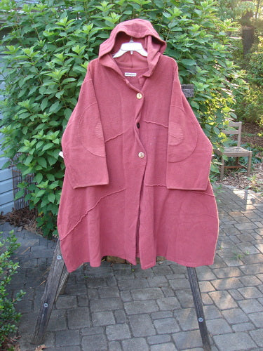 Barclay Celtic Moss Hooded Curve Coat Unpainted Sunset Size 2, featuring a cozy hood, giant circle sleeve patches, and a sweeping A-line flair, displayed hanging outdoors.
