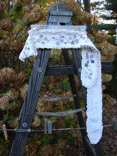 Image: A ladder with a scarf on it, surrounded by trees and plants in autumn. 

Alt Text: Barclay Sash Scarf Floral Berry Vine Orchid OSFA displayed on a ladder amidst an outdoor autumn setting.
