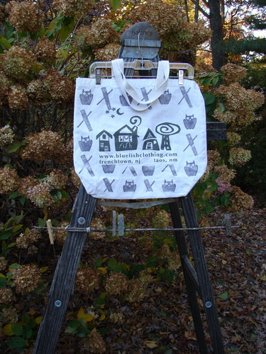 Barclay Promo Tote Bag Shop Locations Owl Natural OSFA displayed on a wooden easel, featuring black and white designs, shorter shoulder strap, generous top opening, and deeper rounded bottom.