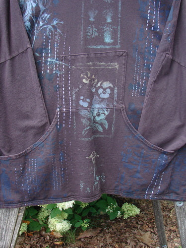 Barclay Cotton Lycra Dolman Roo Pocket Hoodie in Pansy Rose Deep Bark, a relaxed pullover with wide dolman sleeves and a large front kangaroo pocket. The cotton-lycra knit shows a muted plum base with blue botanical and vertical print details, finished in a soft, textured drape.