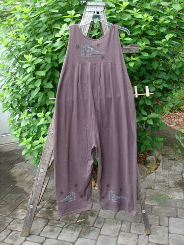 The 1993 Wide Pant Overall Jumper Star Path Travel Redyed Dark Plum Size 1, featuring super wide belled legs and three original front buttons, hangs stylishly on a clothes rack.