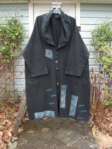 1994 Reprocessed Carriage Coat Forest Path Redyed Edo Black OSFA hanging on a rack, showcasing its oversized vintage buttons, wide collar, and unique patchwork designs. The coat exudes elegance and individuality.