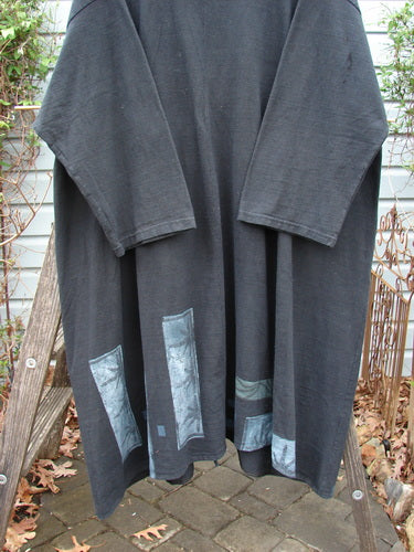 1994 Reprocessed Carriage Coat Forest Path Redyed Edo Black OSFA hangs elegantly on a wooden rack, showcasing its oversized collar, unique hemline, and distinctive Blue Fish vintage buttons.