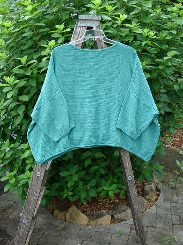Barclay NWT Gauze Square Mariposa Pullover Unpainted Jade OSFA displayed on a wooden rack, highlighting its wide three-quarter sleeves and boxy flowy shape, emblematic of BlueFishFinder's creative, expressive style.