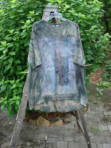 Barclay Tournesol Tunic Wind Script Mottled Green Earth OSFA displayed on a wooden ladder, showcasing its tunic length, drop shoulders, three-quarter sleeves, rounded neckline, and varying hemline.