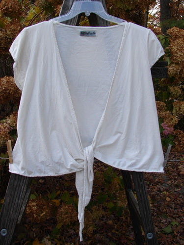 Barclay Cotton Lycra Cap Sleeve Tie Shrug Unpainted Creme Size 2 hanging on a clothesline, showcasing its sleeveless design and deep V-shaped neckline with front tie option.